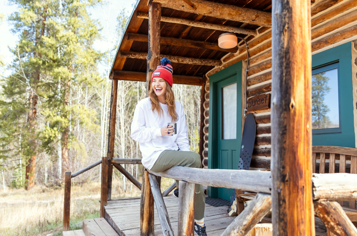 Woman smiling sitting on a wooden cabin porch with trees in the background
