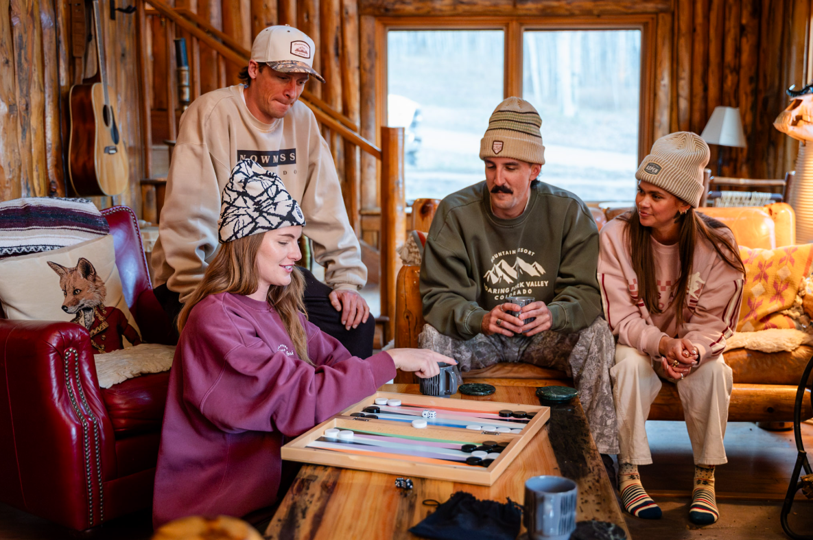 Group of people sitting around a wooden table in a cozy cabin, playing cards.