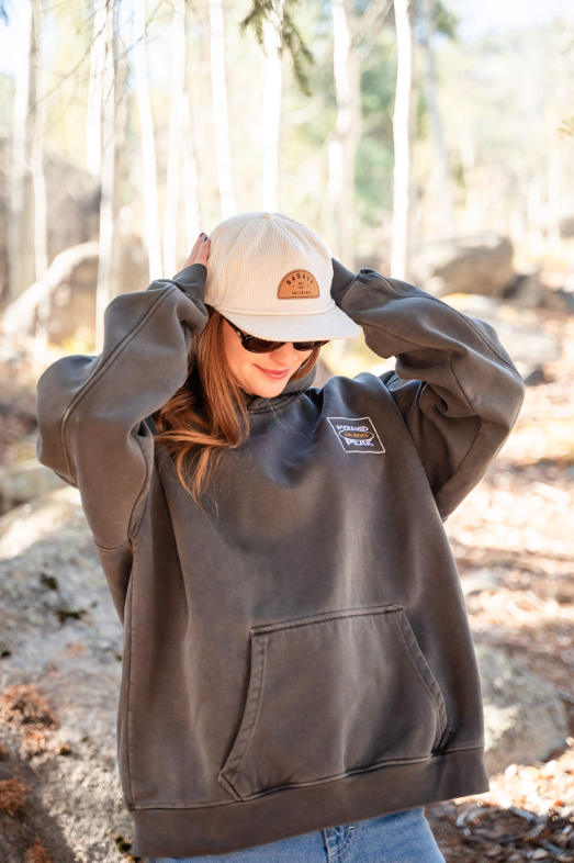 Person wearing a brown hoodie and beige cap in a forest setting