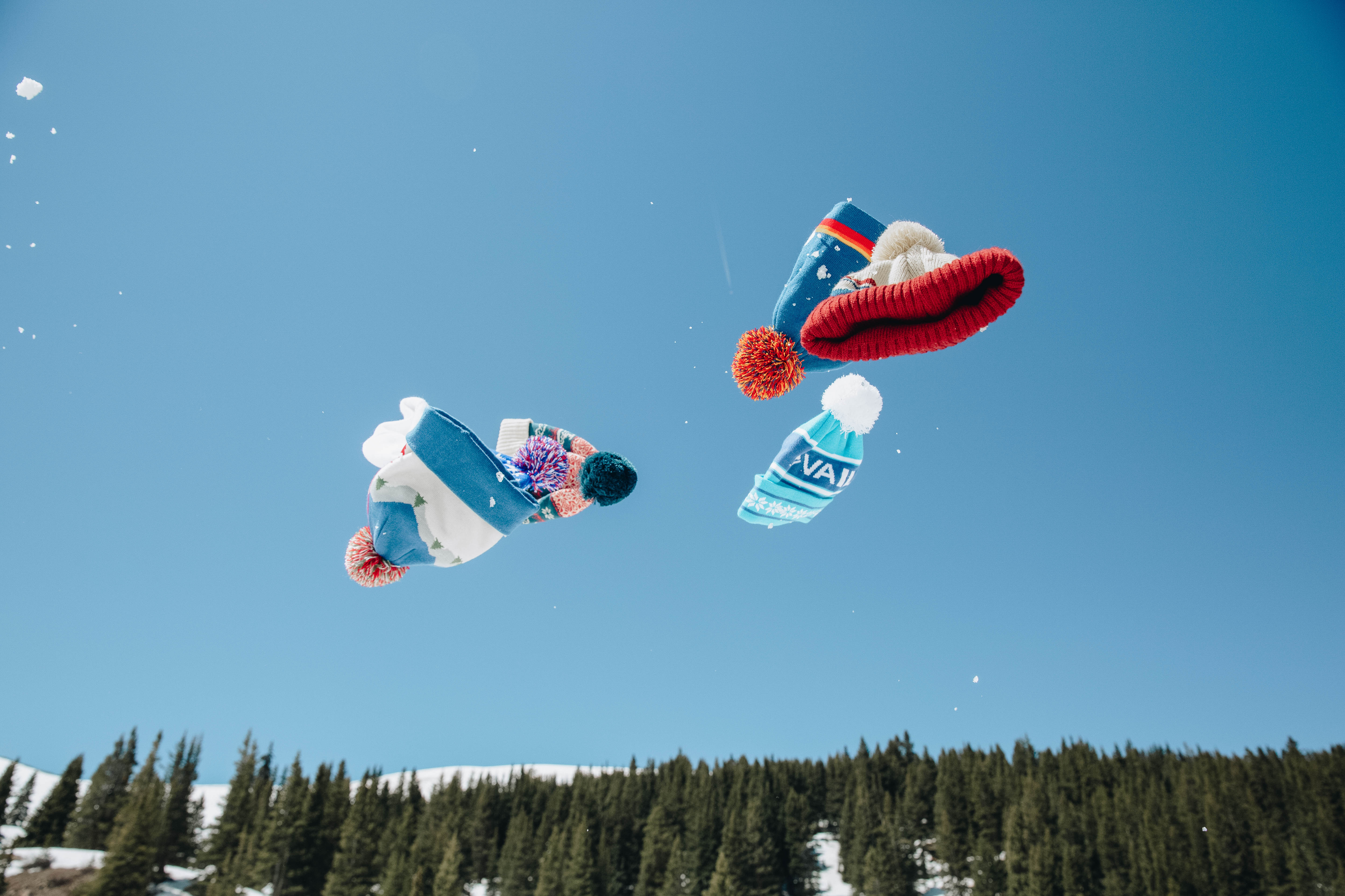 Two colorful kites flying against a clear blue sky with trees below.