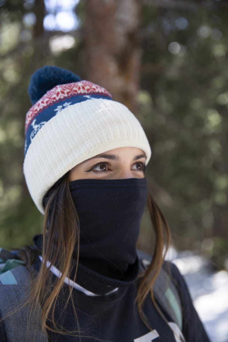 Women wearing a colorful beanie and black face mask in a snowy forest setting